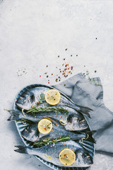 Fresh uncooked dorado or sea bream fish with lemon, herbs, oil, vegetables and spices on concrete background. Top view. Healthy food concept. Copy space. Food pattern