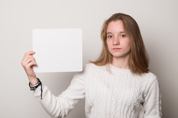 Naklejka premium Positive girl holds a blank poster for text. Schoolgirl with a smile holds a white sheet for text.