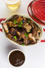 Grilled pork belly in a red bowl with barbecue salce and beer in white background seen from above