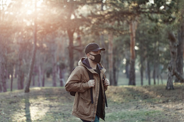  Man in medical mask with backpack in jacket and cap walking in forest