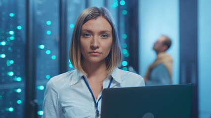Female server technician doing checkup operations on laptop computer coworking in cyber server room. Portrait of professional woman engineer in data center interior.