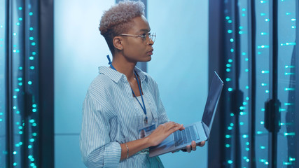 Professional african woman administrator running data center backups operation on open server rack...
