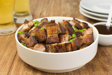 Grilled pork belly in a white bowl with barbecue salce and beer in wood pub table background