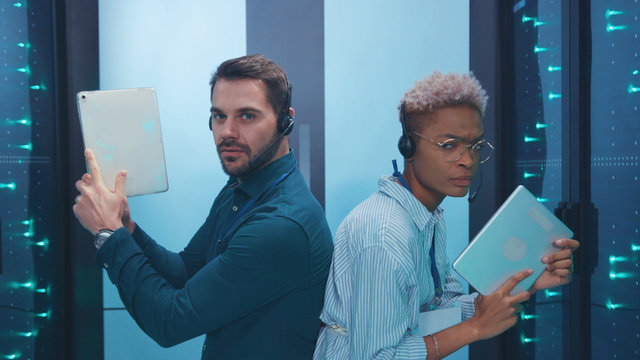 Professional multi-race armed spies on secret operation sneaking in server room walking aiming tablets like guns working in team. Data center. Fun concept.