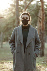 Woman in medical mask posing on the camera on the trees background. Girl uses a protective mask against a viral infection. Outdoor. people do not obey the call