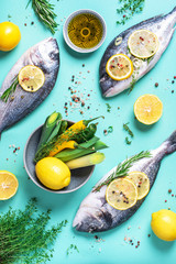 Fresh raw sea dorado fish with lemon slices, herbs, oil, salt, pepper, greens on blue background. Top view. Healthy food concept. Copy space. Food pattern