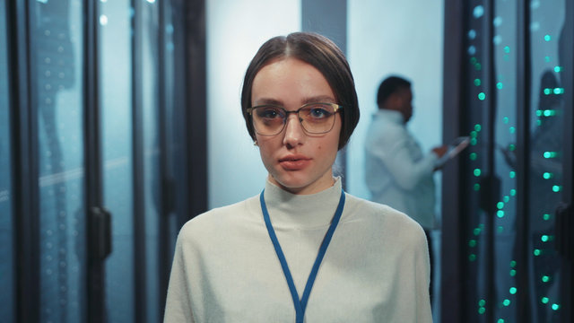 Attractive smart caucasian woman data center engineer working on digital laptop typing network data standing at row of operational server rack cabinets. Close-up.