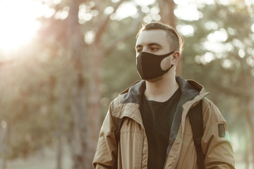 medium shot portrait of man in medical mask. Adult person in black mask standing in park and...