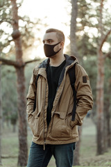 medium shot portrait of man in medical mask. Adult person in black mask standing in park and looking sideways
