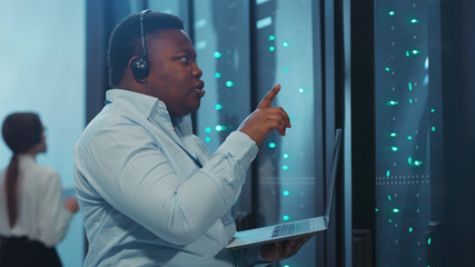 Busy african IT service support technician talking performing working tasks on notebook inspecting...