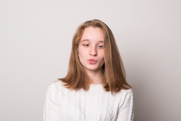 Obraz premium Emocjonalna nastolatka krzywi się. Studio obraz cute uśmiechnięta młoda dziewczyna na szarym tle.