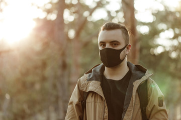 Close up portrait man in medical mask. Young man stands on the trees background and looking at camera. Outdoor. Health protection and care. Virus