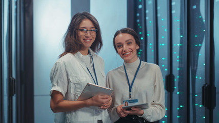 Couple of smart women IT technicians checking open rack server cabinet checking updating hardware cooperating in futuristic digital room of data center.
