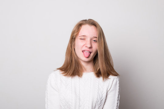Cheerful girl teenager with tongue hanging out. Studio image of a cute smiling young girl on a gray background.