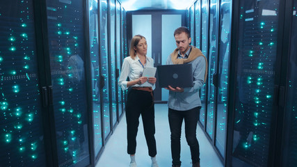 Couple of server engineers cooperating in high tech data center. Male and female technicians...