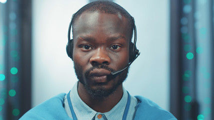 Portrait of african young man IT specialist wearing headphones standing in technological server room. Data center. Cyber security.