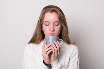 Charming girl with a mug of tea. Cute teenager girl with blond hair holds a mug. Girl drinks from a mug.