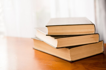 three hardcover books are stacked on a wooden table