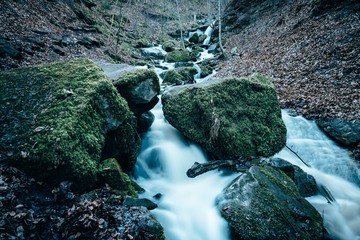 Green moss-covered rocks at rushing waterfall in forest