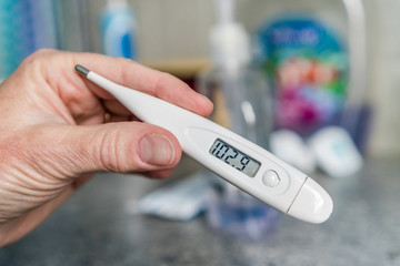 Close-up of hand holding thermometer measuring a high fever.