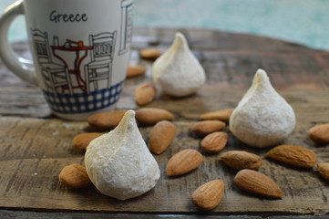 Traditional greek almond cookies, amygdalota with powdered sugar, almonds and cup of coffee on the wooden background - obrazy, fototapety, plakaty