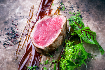 Gebratenes dry aged Rinderfilet Medaillon Steak natur mit Salat und Gewürzen als closeup auf einem rustikalen Modern Design Teller