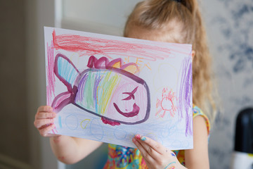Childrens creativity. Little child girl draws with wax pencils at home. The concept of distance...