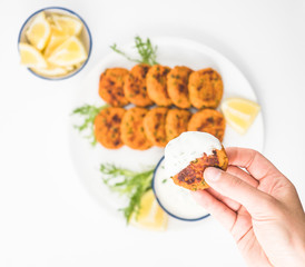 Close up hand holding a fish cake over a plate with more fish cakes.