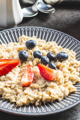 Plate of oatmeal porridge with strawberries and blueberries.