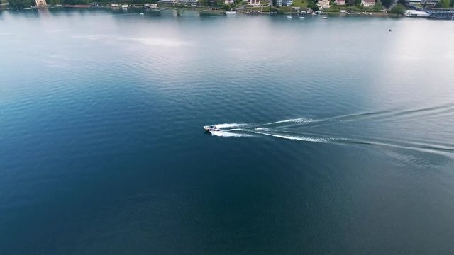 Aerial drone tracking shot of a speed boat and a man waterskiing doing water sports in Velden Am Worthersee lake, Austria on a beautiful sunny day mountain view 