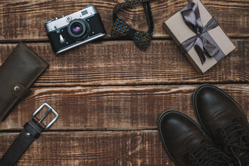 Fototapeta na wymiar Gift box for father's day with men's accessories bow tie, wallet, retro camera, belt and leather shoes on a wooden background. Copy space. Flat lay.