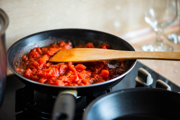 Tomato sauce with cut tomatoes, with wooden spatula  in the pan. On the dark glass cooker. Food preparation background