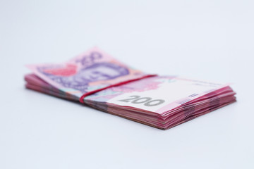 A lot of new banknotes in denominations of 200 Ukrainian hryvnias bandaged with an elastic band isolated on a white background with shadow. European money exchange. Ukraine currency. Selective focus