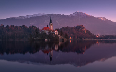 Beginning Of The Day At Lake Bled In Winter, Slovenia. Pinky Sunrise With Perfect Reflection Of Julian Alps And St. Marys Church Of The Assumption.Slovinian Landscape With Bled Castle ( Blejski grad )