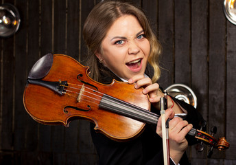 Charismatic girl with a violin on a dark background. Young violinist. Cheerful teenage girl