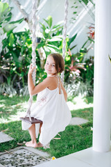Portrait of a little brunette girl sitting on swings in a courtyard