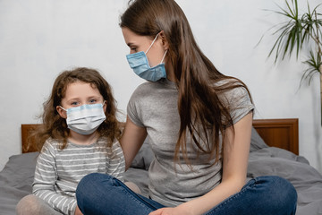 Compassionate caring attentive mommy having trustful conversation with daughter wearing medical face mask sitting on bed. COVID-19 pandemic infectious disease outbreak protection, healthcare concept