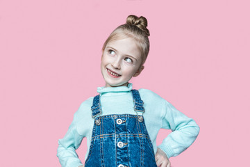The little girl smiles. A little girl with blond hair looks up joyfully and playfully against a pink isolated background