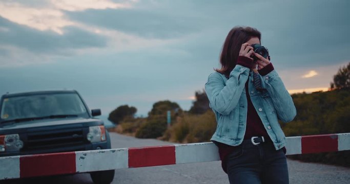 Cute young female photographer with vintage film camera taking photos outdoors while going to road trip in Europe, slow motion