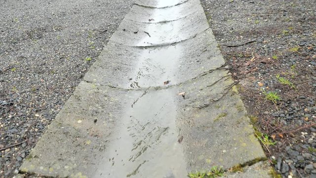 Rain water movement in concrete drna. Water flows down from ruptured sewer pipe.  Streams of water flows on to road from crack in ground