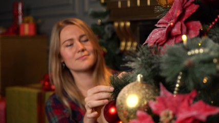 Young beautiful girl or woman in a red plaid shirt decorates a Christmas tree for Christmas or New Year.