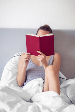 Frau liest rotes Buch im Bett
