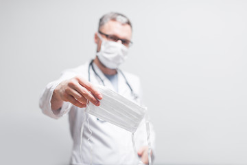 doctor in a coat in a medical mask holds a mask on the background