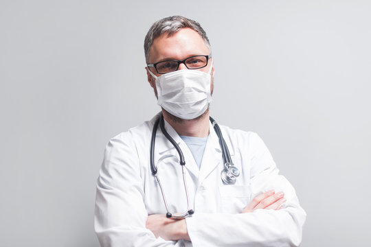 doctor in a lab coat stands in a medical mask on a light background on a bright day