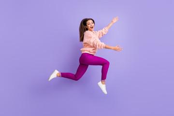 Fototapeta na wymiar Full length profile photo of cheerful lady jumping high rushing friends meeting raise hands to empty space wear casual fluffy pullover pants shoes isolated purple color background