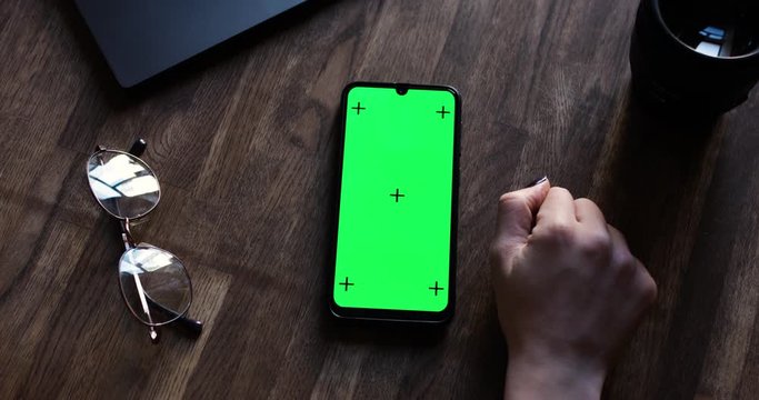 The View From The Top. Phone with a Green Screen and Tracking Dots on the Table. Chromakey. The Girl's Hand Scrolling The Screen. Concept for Ads and Apps