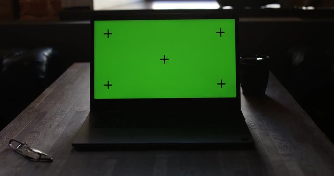 Laptop with green screen and Tracking Dot. Dark office. Dolly in. Perfect to put your own image or video. Track with perspective corner pin. Green screen of technology being use. 4K
