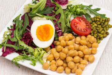 Multicolored vegetable mix, chickpeas, mung bean, egg and tomato in black plate