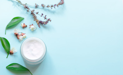 Cosmetic cream in a jar and flowers on a light blue background. Concept natural cosmetics, beauty, aromatherapy, skincare. Top  view and copy space flay lay