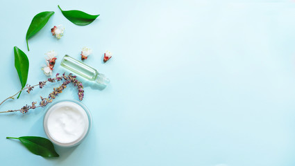 Lavender essential oil and cosmetic cream in a jar with flowers on a light blue background. Natural cosmetics, beauty, aromatherapy, skincare concept. Top  view and copy space flay lay.